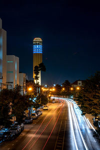 Illuminated city street and roi et tower against sky at night