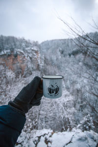 Person holding ice cream cone against sky during winter