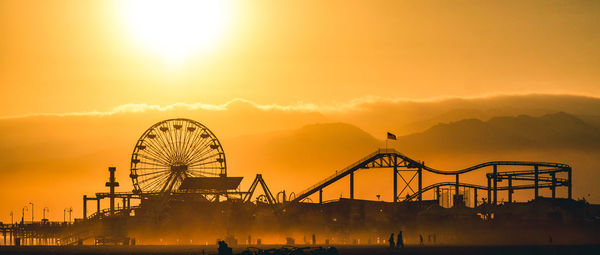 Silhouette amusement park against sky during sunset