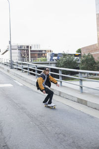 Man skateboarding on street in city against sky