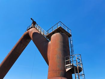 Low angle view of electricity pylon against clear blue sky