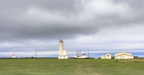 Lighthouse on field by buildings against sky