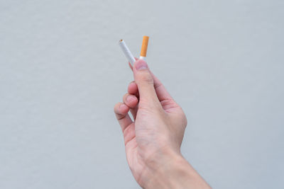 Close-up of hand holding cigarette against white background