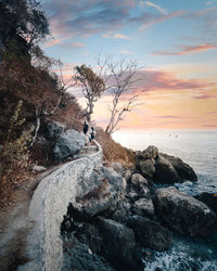 Man on rock by sea against sky during sunset