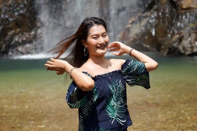 Portrait of smiling young woman standing against waterfall