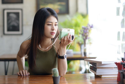 Young woman with camera sitting on table at restaurant