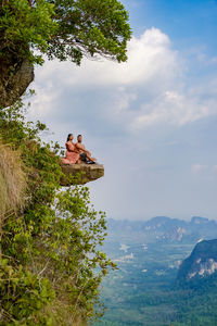 People sitting on mountain by sea against sky