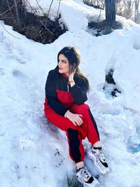 Portrait of young woman sitting on snow covered field