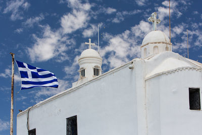 Low angle view of greek flag waving by church against cloudy sky
