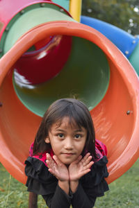 Portrait of girl lying on slide in playground