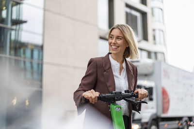 Happy young businesswoman with e-scooter in the city