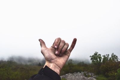 Cropped image of hand showing shaka sign on field against sky