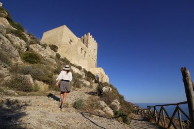 Rear view of woman walking towards old ruin by sea against clear sky
