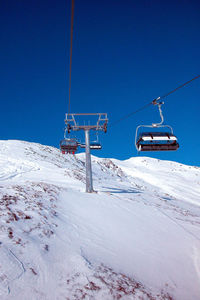 Chairlift in alpine ski area, clear blue sky, mountain slope covered in snow