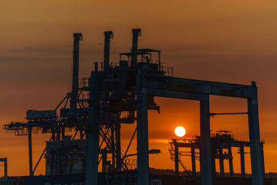 Silhouette cranes against sky at sunset