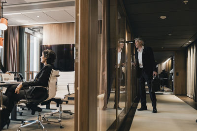 Curious businessman looking through glass wall at colleagues in board room during meeting