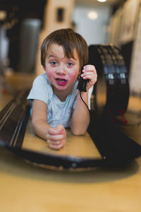 Portrait of boy holding remote control while lying down amidst toy racetrack