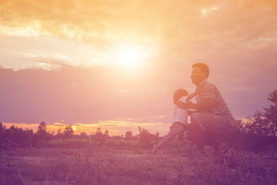 Father and daughter on land against sky during sunset