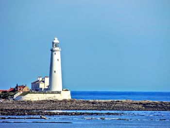 Lighthouse by sea against clear sky