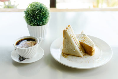 Close-up of sandwich in plate and a cup of brewed coffee on table