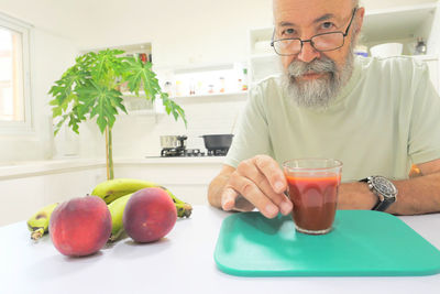 Senior man drinking tomato juice in the kitchen 