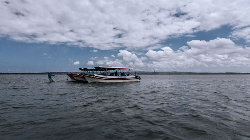 Boats in sea against cloudy sky