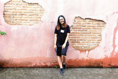 Full length portrait of woman standing against wall