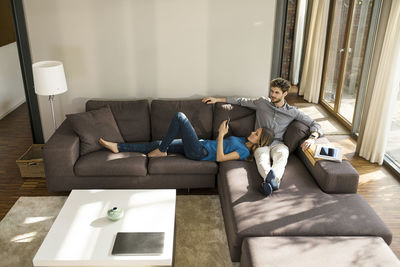 Couple with tablet and smartphone relaxing on sofa in modern living room at home