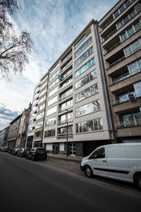 Cars on road by building in city against sky