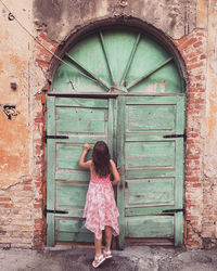 A young girl on tip toe peers through an old door of a building 