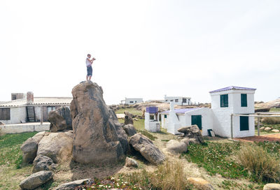 Low section of man standing on rock against clear sky