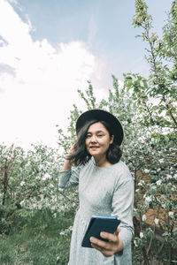 Beautiful asian girl in a hat takes a selfie on a smartphone in a blooming garden