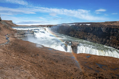 Tourists exploring beautiful gullfoss waterfall in golden circle against sky