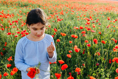 High angle view of girl standing in the field of poppies and tasting fresh peas