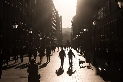 Silhouette people walking on street amidst buildings on sunny day