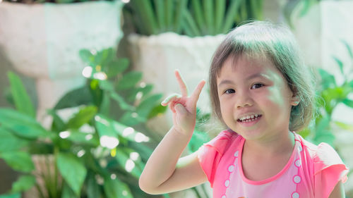 Happy charming 4 years old cute baby asian girl, child raising her 2 fingers up, looking at camera.