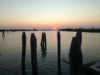 Wooden posts in sea against sky during sunset