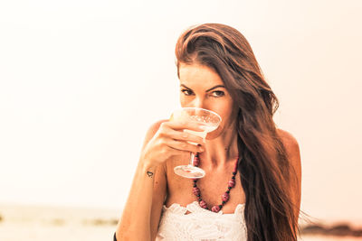 Portrait of mature woman holding drink at beach against sky