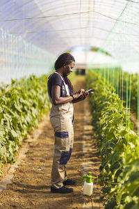 Female farmer using digital tablet while standing at greenhouse