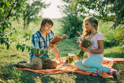 Happy woman sitting on field against trees