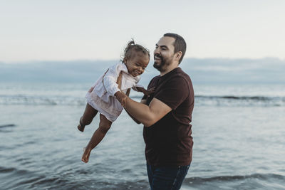 Dad and daughter playing in the ocean at dusk