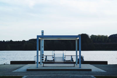 Empty swimming pool by lake against sky