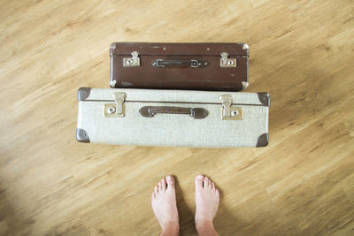 Low section of person standing by luggage on hardwood floor