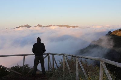 Rear view of man standing at observation point against cloudscape