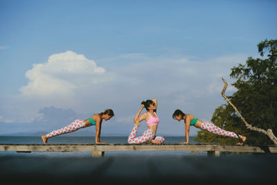 Three asian woman taking yoga pose on beach pier