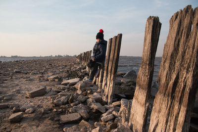 Rear view of man on rock at beach against sky