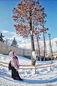 Woman standing by tree on field against sky during winter