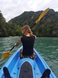 Rear view of woman in boat on lake against mountain