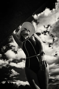 A portrait of a woman in a swimsuit, hat and sunglasses in summer on the riverbank against the sky