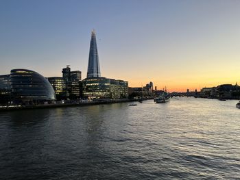 Buildings by river against sky during sunset